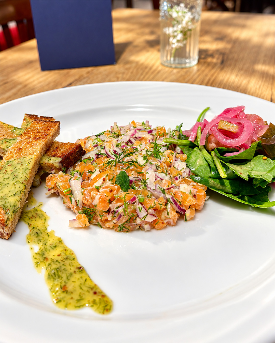 Tartare de saumon aux herbes servi avec salade et pain toasté